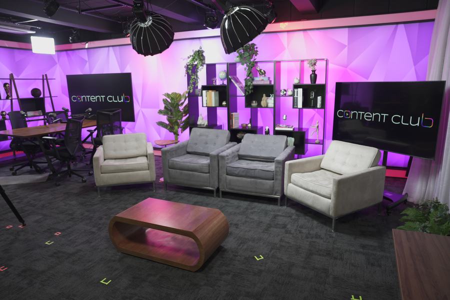 Cenário lounge do Content Club com poltronas, estante decorada e telão de identidade visual